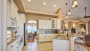 A spacious kitchen with white cabinetry, a granite countertop, and a central island with bar stools.