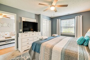 Une chambre à coucher avec un lit, une commode, une télévision et un ventilateur de plafond.