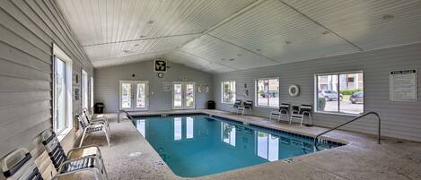 An indoor swimming pool with a tiled floor, benches along the sides, and a sign indicating pool rules.