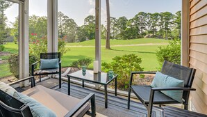 Eine überdachte Terrasse mit Gartenmöbeln, einem Glastisch und Blick auf einen Golfplatz.