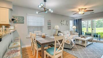 A dining area with a wooden table, chairs, and a ceiling fan. There is a window with blinds and a view of the outdoors.