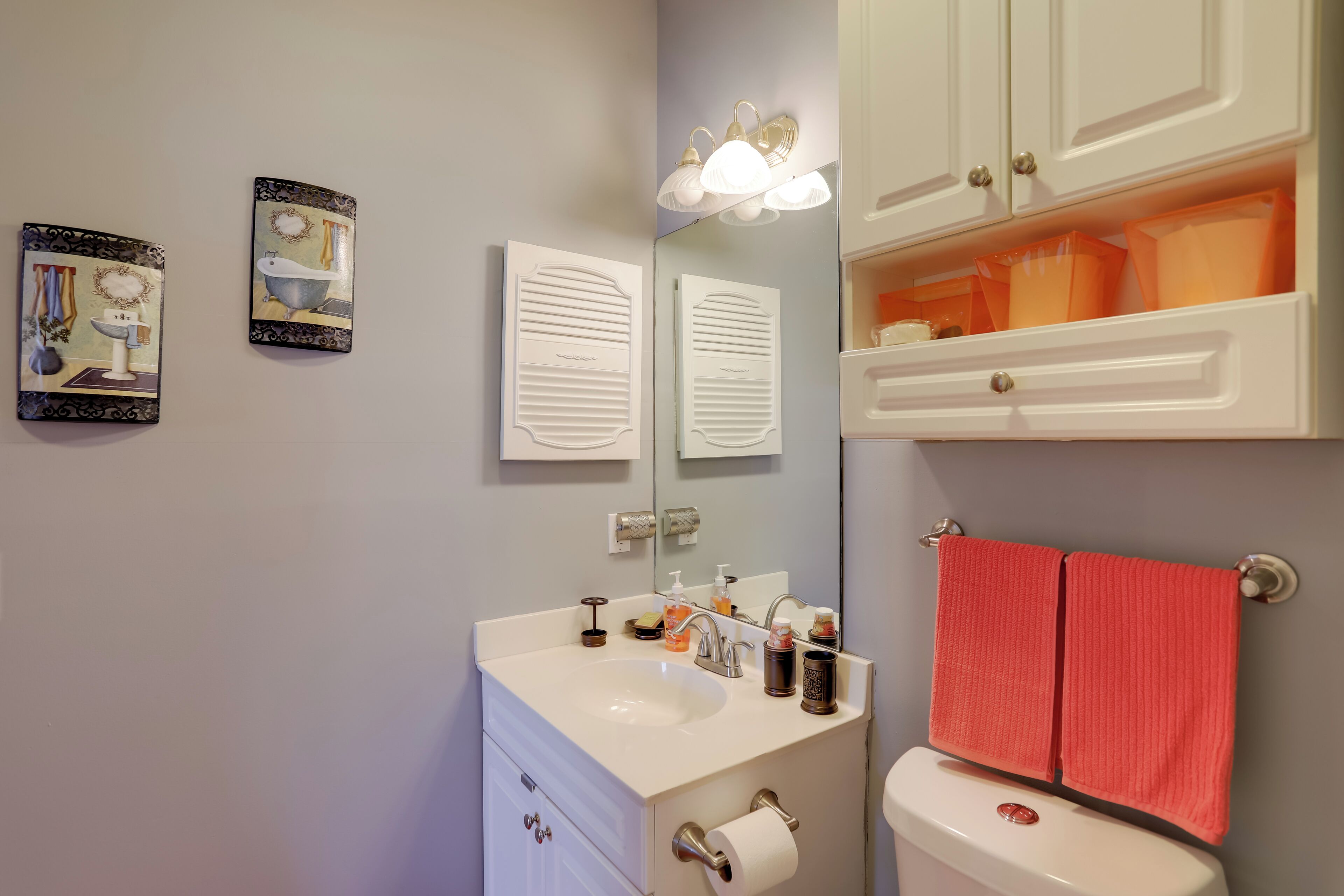 Un bagno con lavandino bianco, specchio e water. Due asciugamani sono appesi al muro.