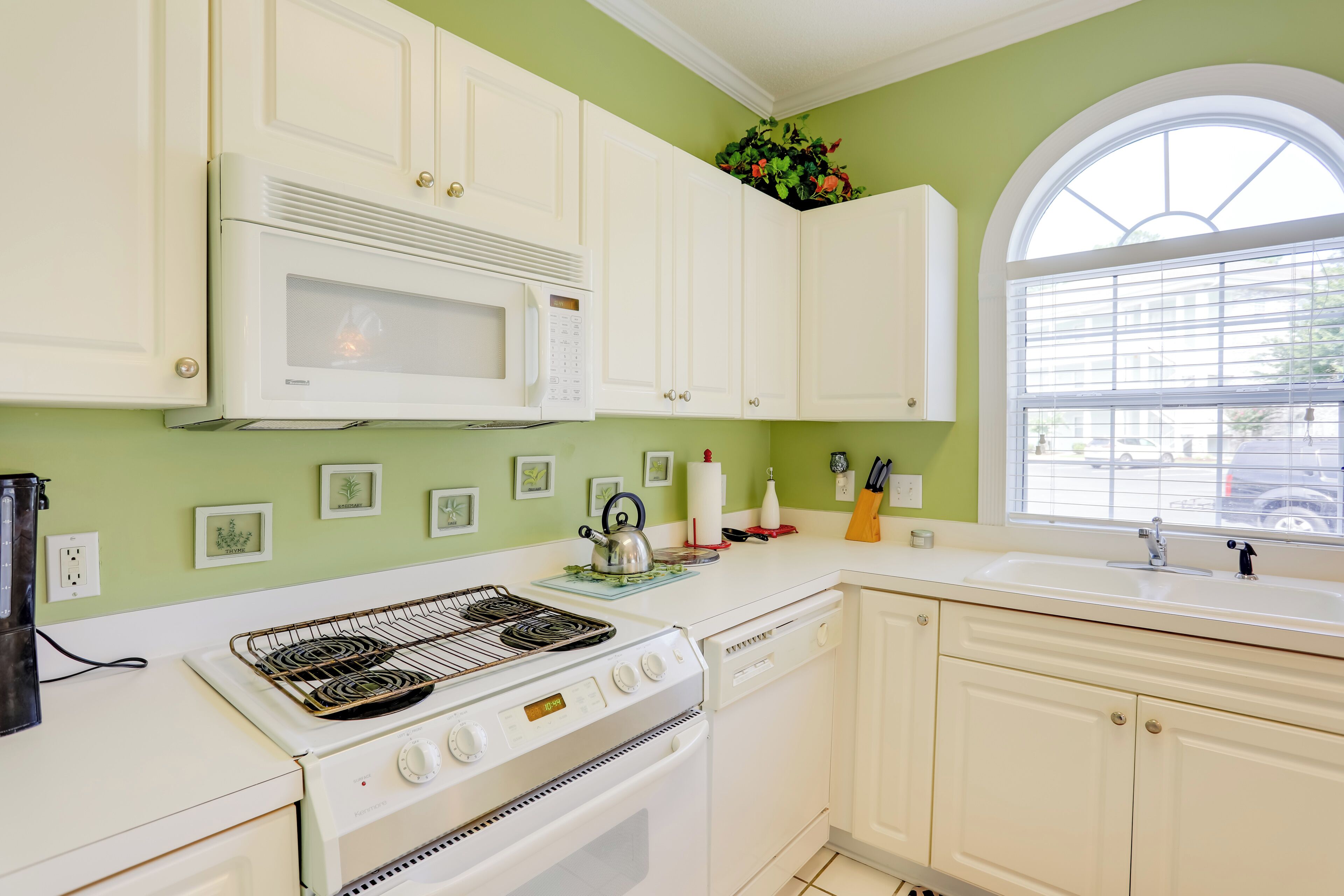A kitchen with white cabinets, a microwave, a stove, and a sink.