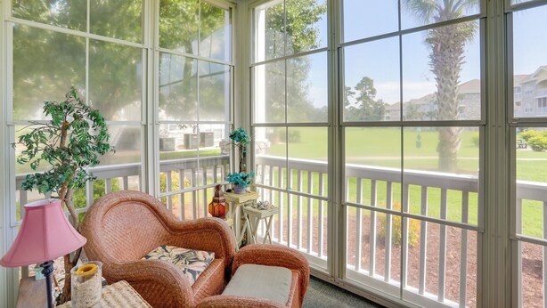 A sunroom with wicker furniture, a lamp, and a view of a green lawn and buildings. - 2 Mi to Broadway at the Beach: Myrtle Beach Condo (Myrtle Beach)