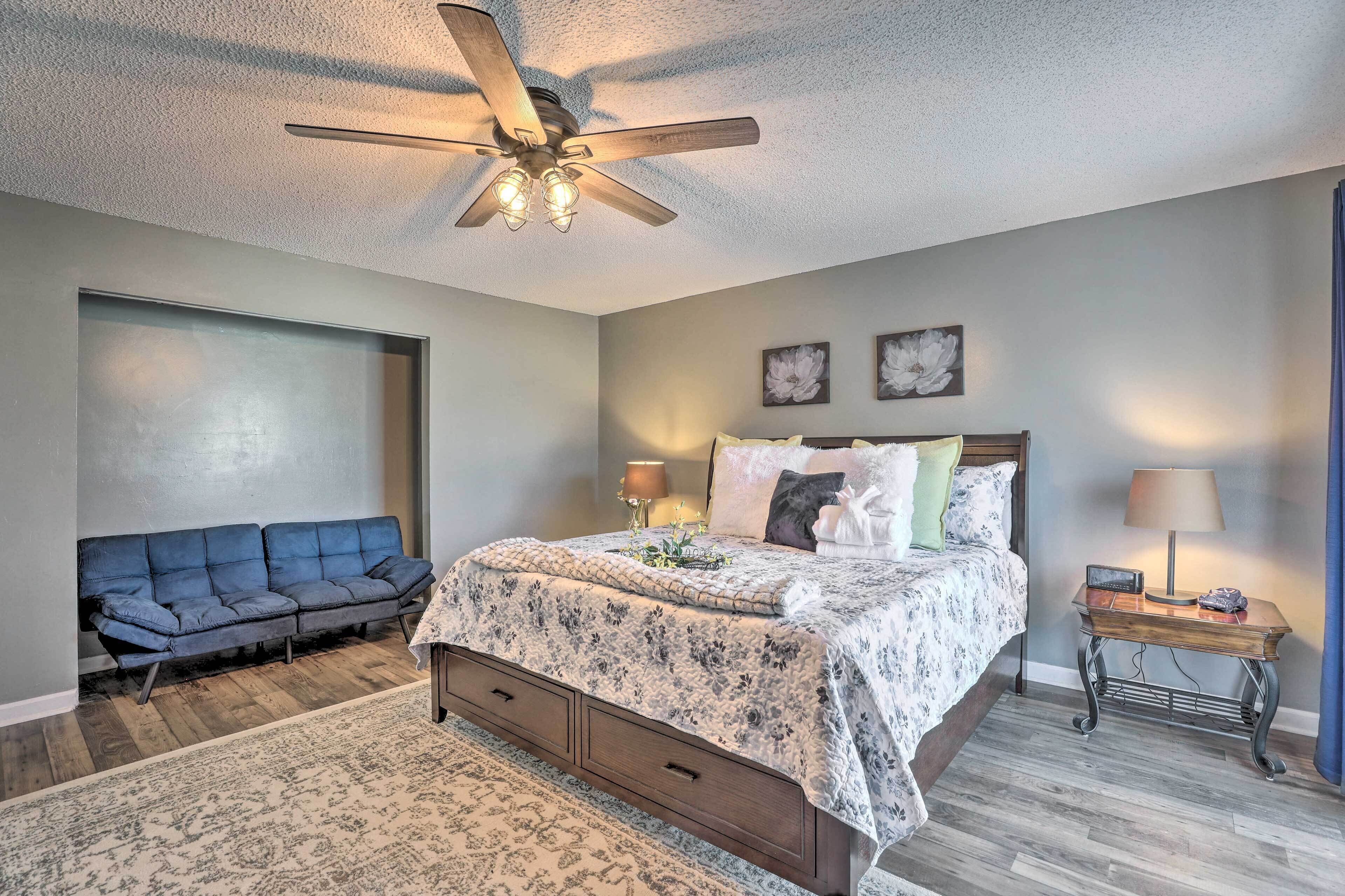 A bedroom with a bed, a blue sofa, a wooden nightstand, and a ceiling fan.