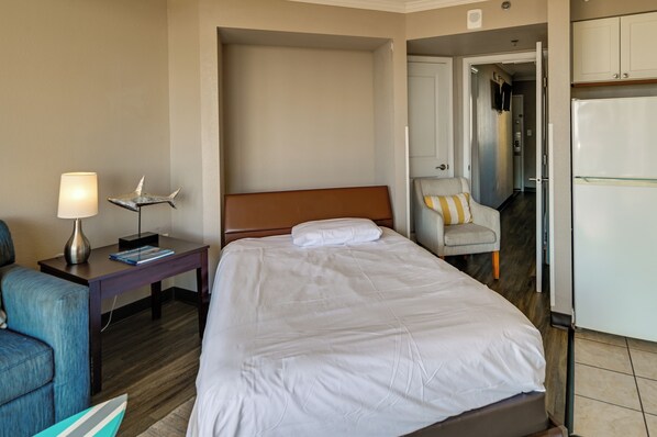A hotel room with a bed, a nightstand with a lamp, a chair, and a refrigerator. - Oceanfront Condo w/ Pool Access in Myrtle Beach! (Myrtle Beach)