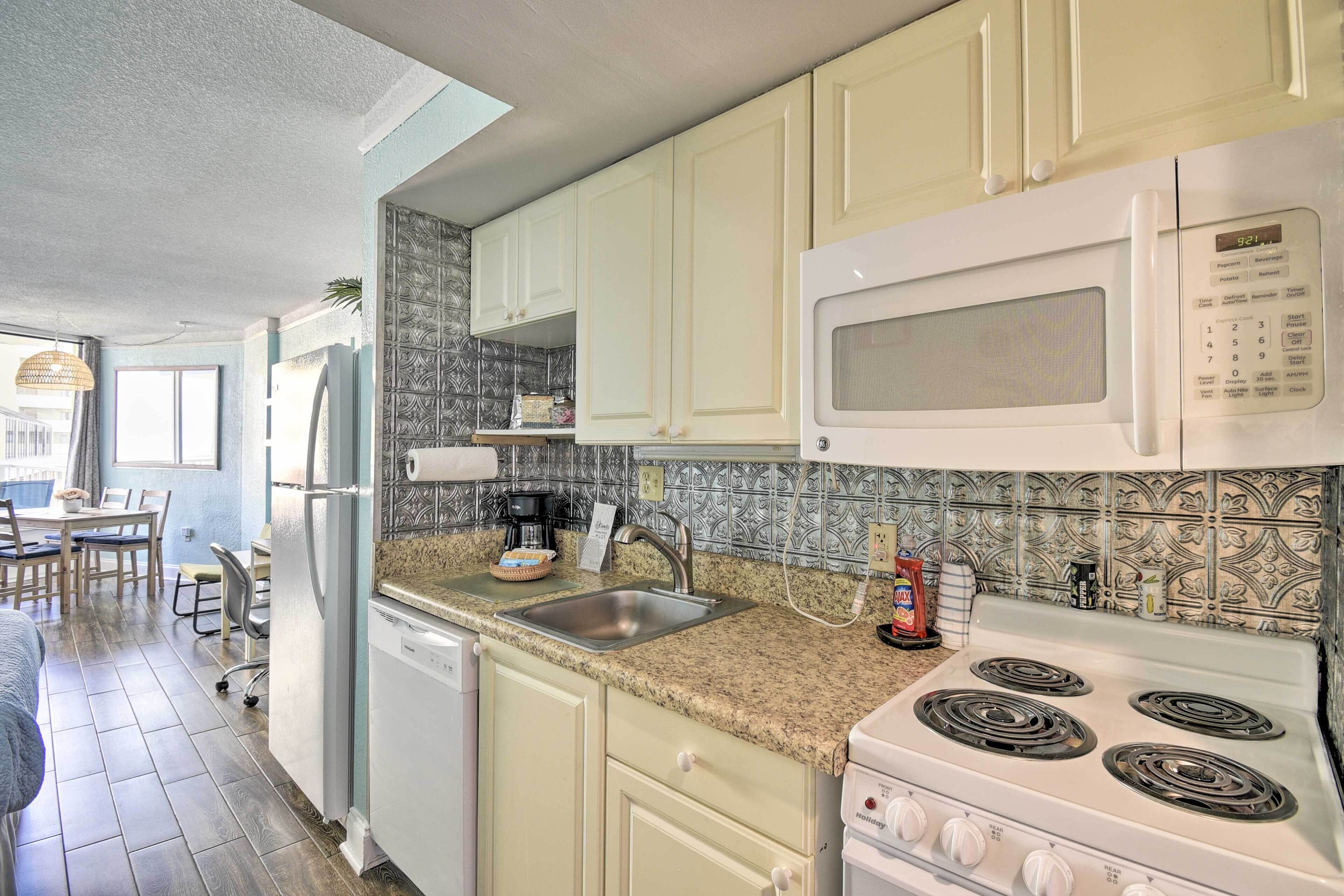 A kitchen with white cabinets, a granite countertop, a microwave, a stove, and a sink.