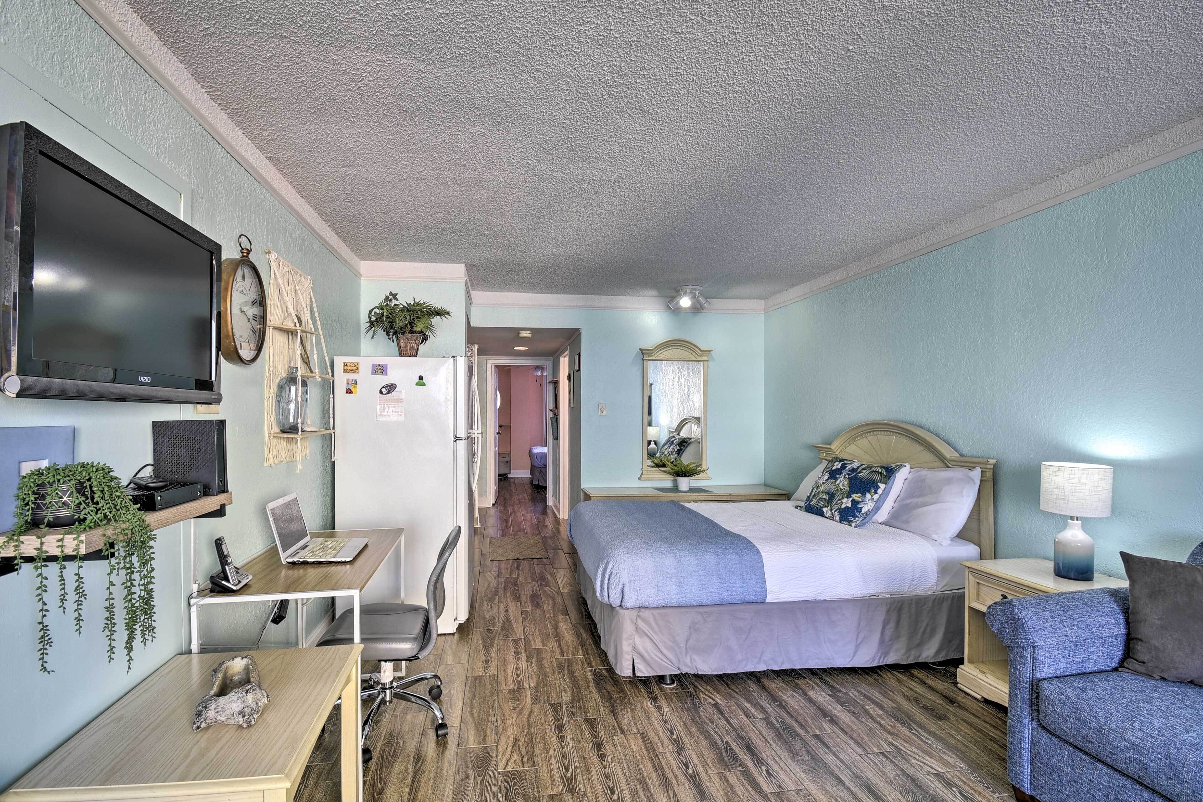 A bedroom with a bed, a desk with a laptop, a TV, and a chair.