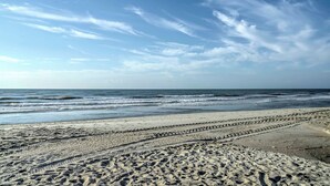 Ein Strand mit deutlich sichtbaren Spurren von Reifen und Fußabdrücken im Sand, die zum Meer führen.