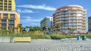 Ein Strandhotel mit mehreren Balkonen, Palmen und einem Sandstrand.