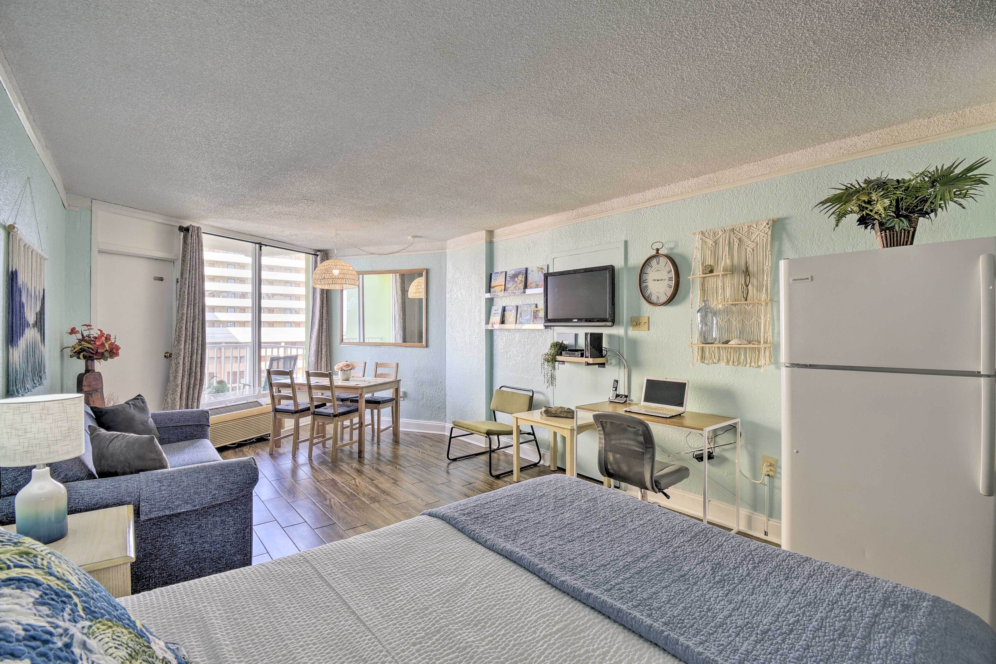 A modern room with a bed, a desk, a chair, a television, and a refrigerator.