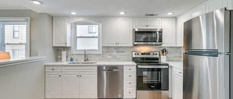 Una cocina moderna con muebles blancos, electrodomésticos de acero inoxidable e iluminación empotrada en el techo.