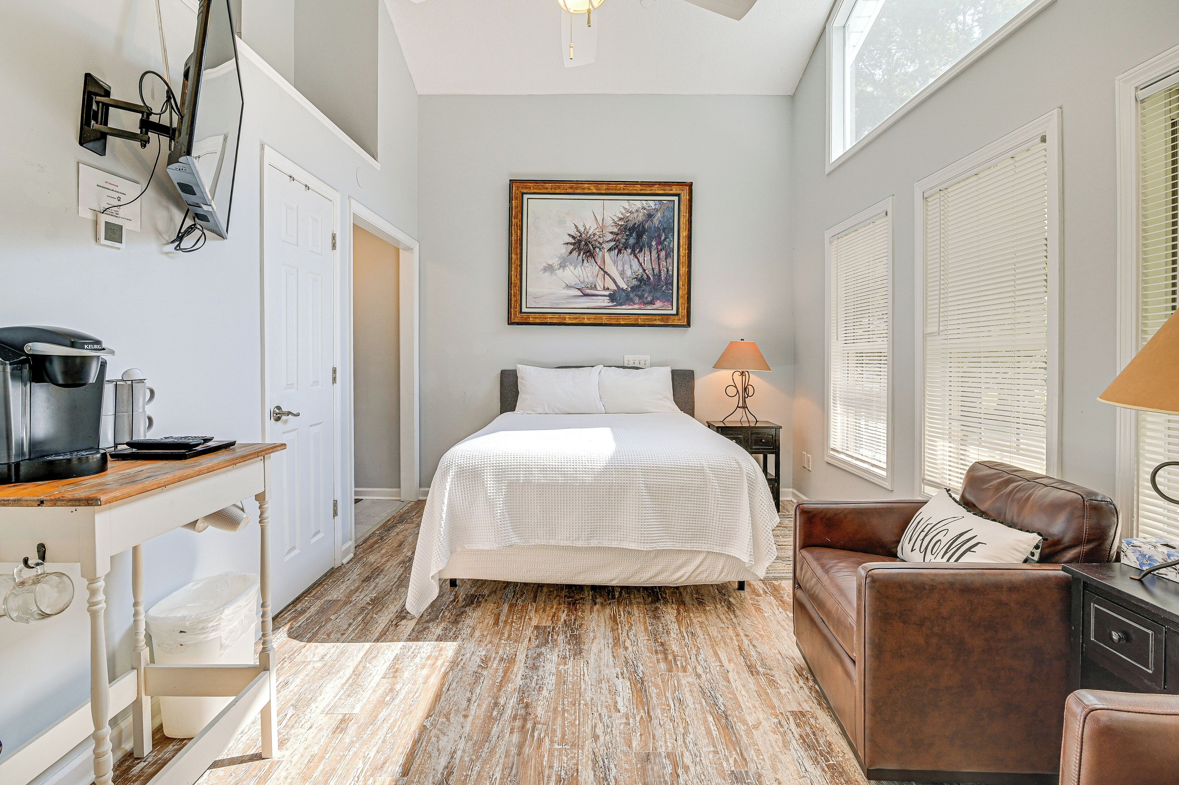 A bedroom with a bed, a desk with a coffee maker, a couch, and a painting on the wall.