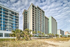 A high-rise hotel with multiple balconies, a beach in the foreground, and palm trees. - Oceanfront Myrtle Beach Rental w/ Pool! (Myrtle Beach)