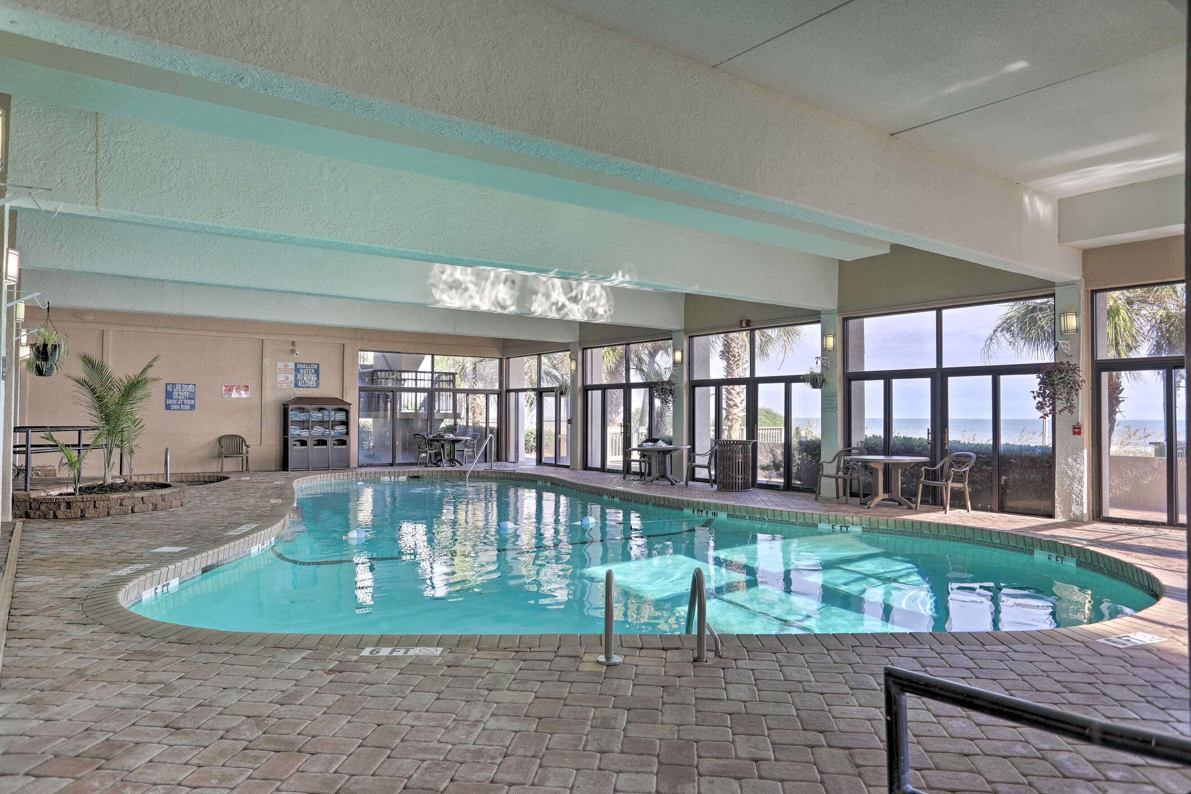 An indoor swimming pool with clear glass walls, a tiled floor, and a view of the ocean.