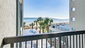 A balcony with a view of the beach, palm trees, and a parking lot. - Oceanfront Myrtle Beach Rental w/ Pool! (Myrtle Beach)