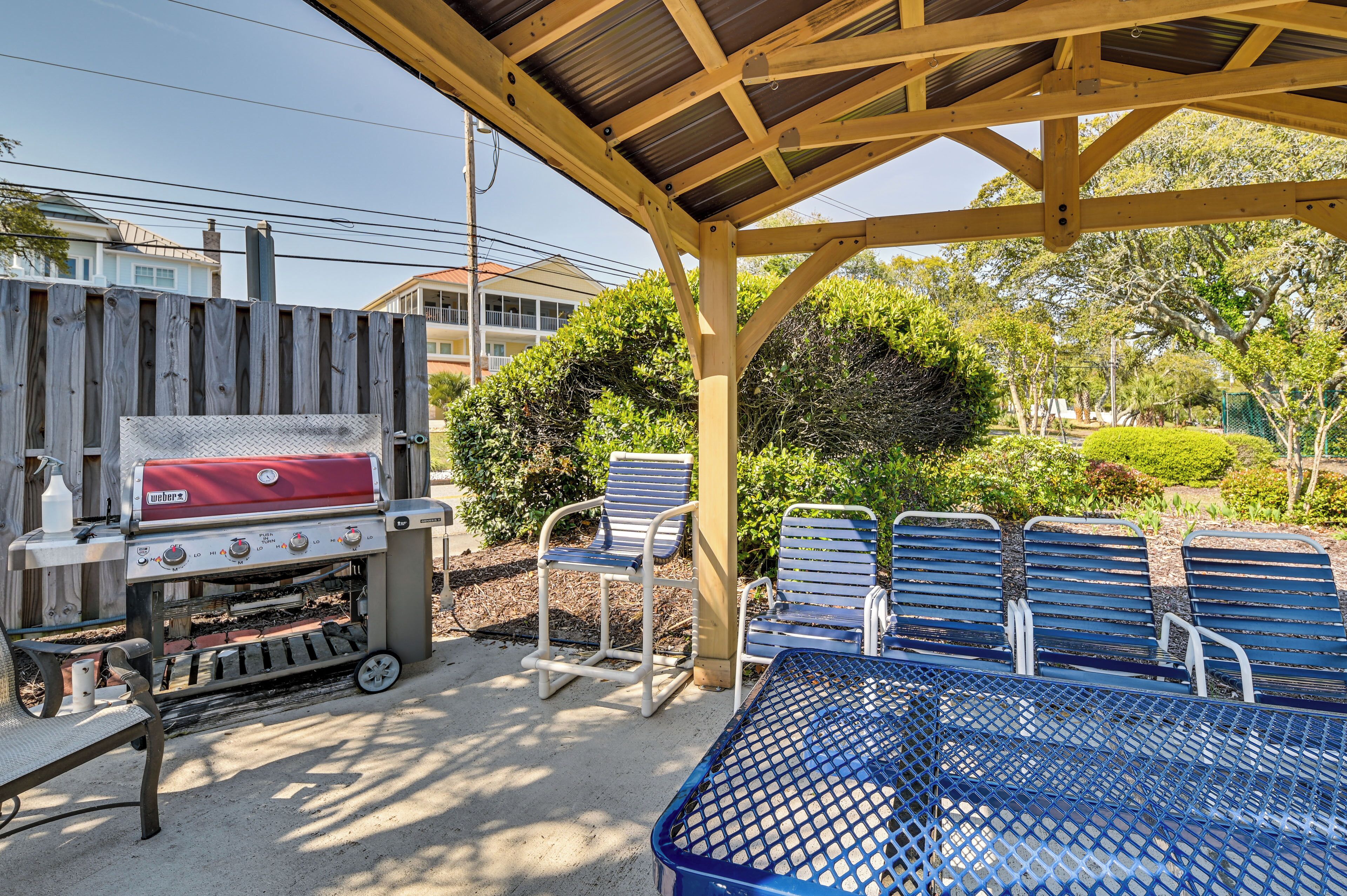A covered outdoor area with a barbecue grill, metal chairs, and a table.