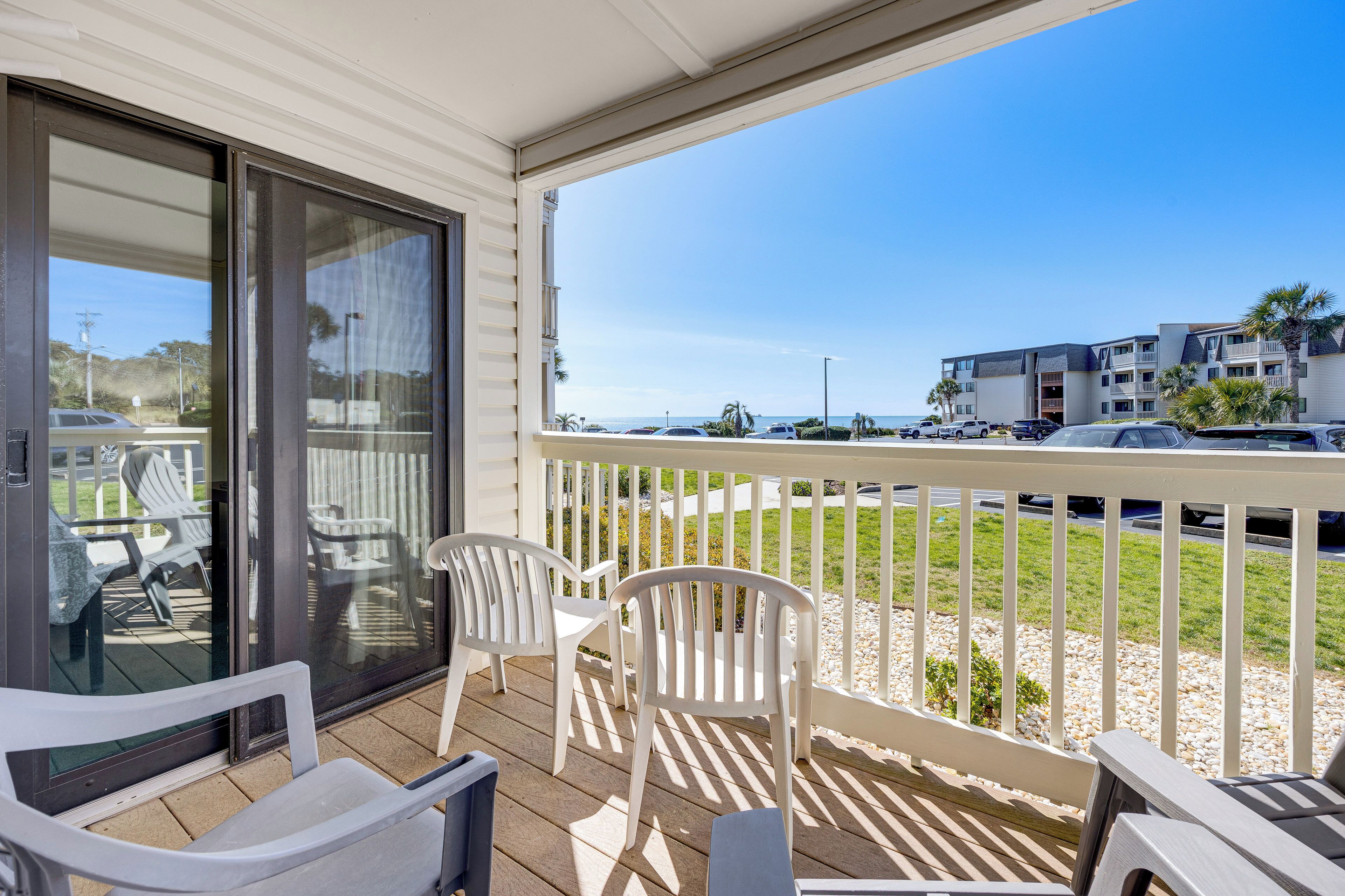 A covered outdoor area with a view of the beach, a pool, and a building in the background.