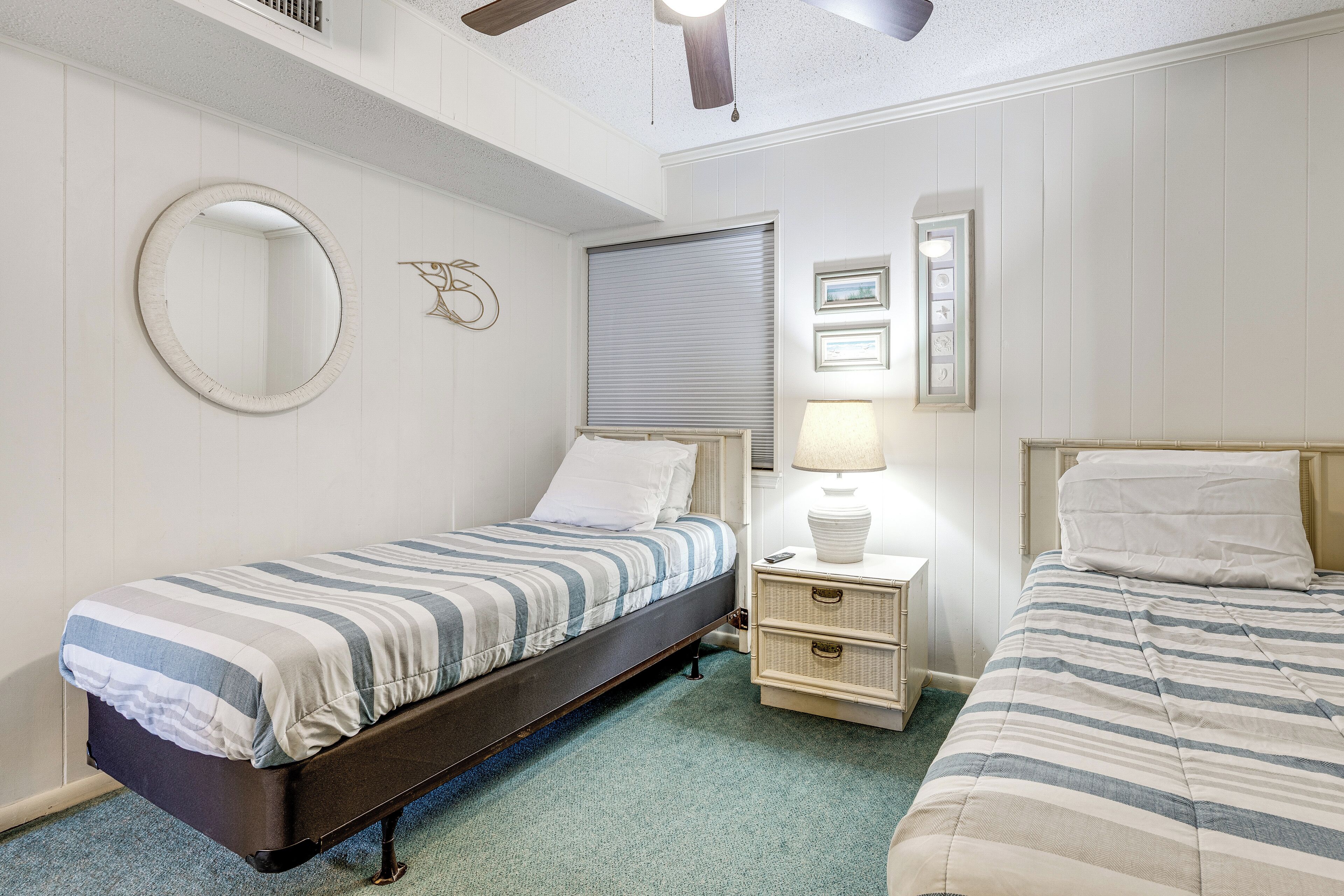A bedroom with two beds, a round mirror, a bedside lamp, and a window with blinds.