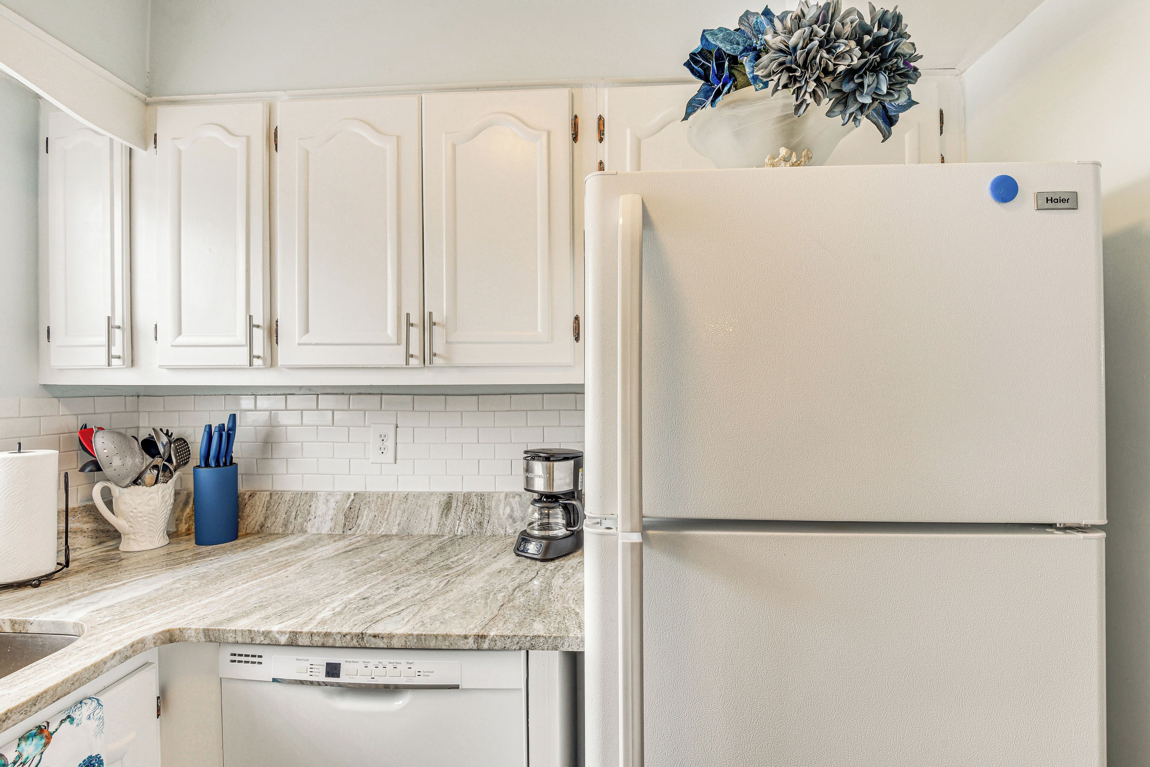 A kitchen with white cabinets, a white refrigerator, a coffee maker, and a dishwasher.