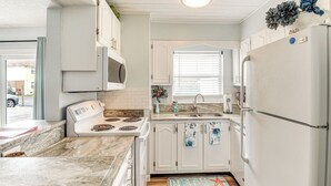 Ett kompakt kök med vita skåp, en spis, en mikrovågsugn och ett kylskåp.