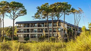 Un hôtel à plusieurs étages, doté de balcons et d’un toit plat, entouré de grands arbres et de zones verdoyantes.