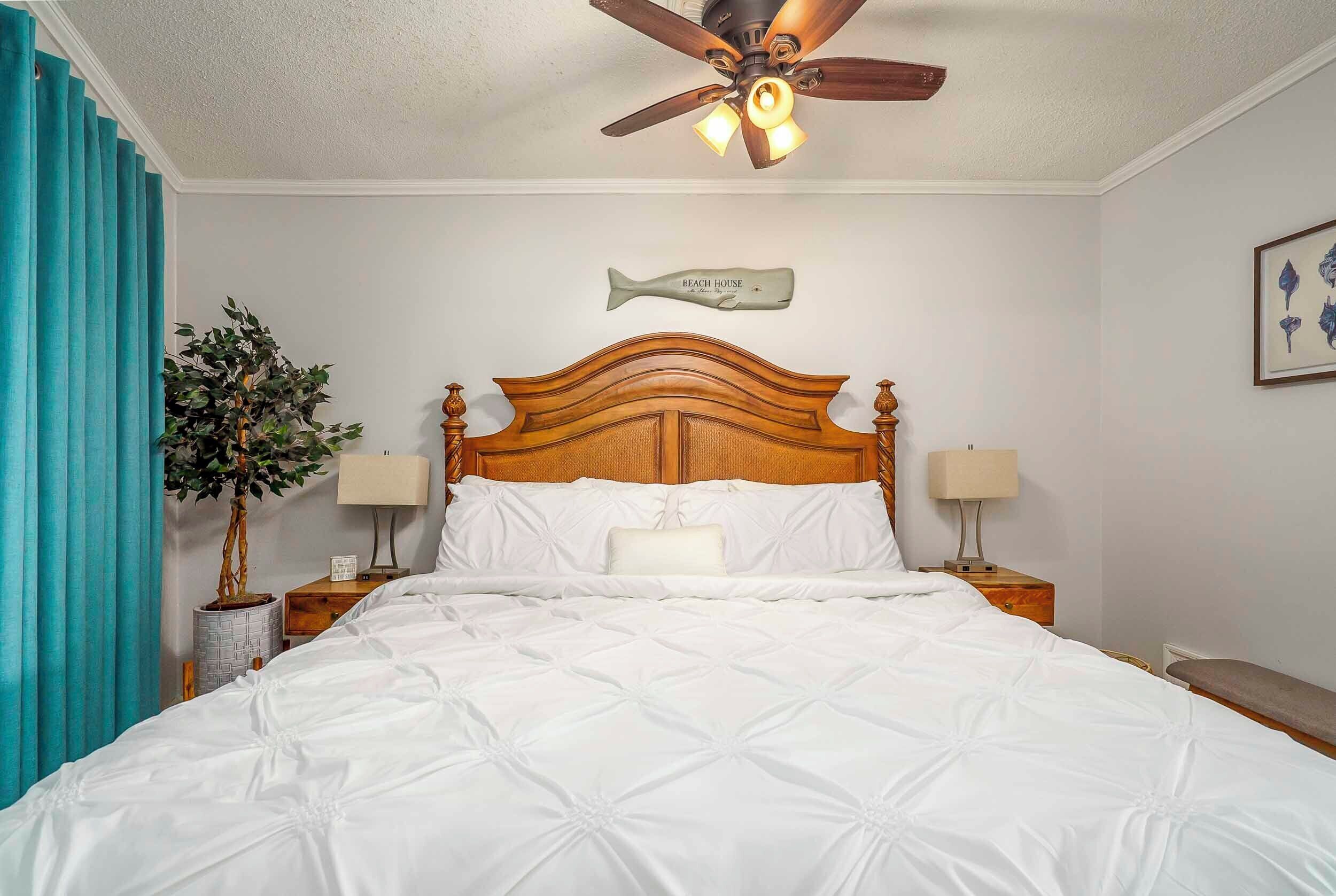 A neatly made bed with a wooden headboard, a ceiling fan, and a wall-mounted fish decoration.