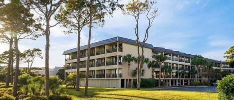 A multi-story hotel with a flat roof, balconies, and a well-maintained lawn with trees.