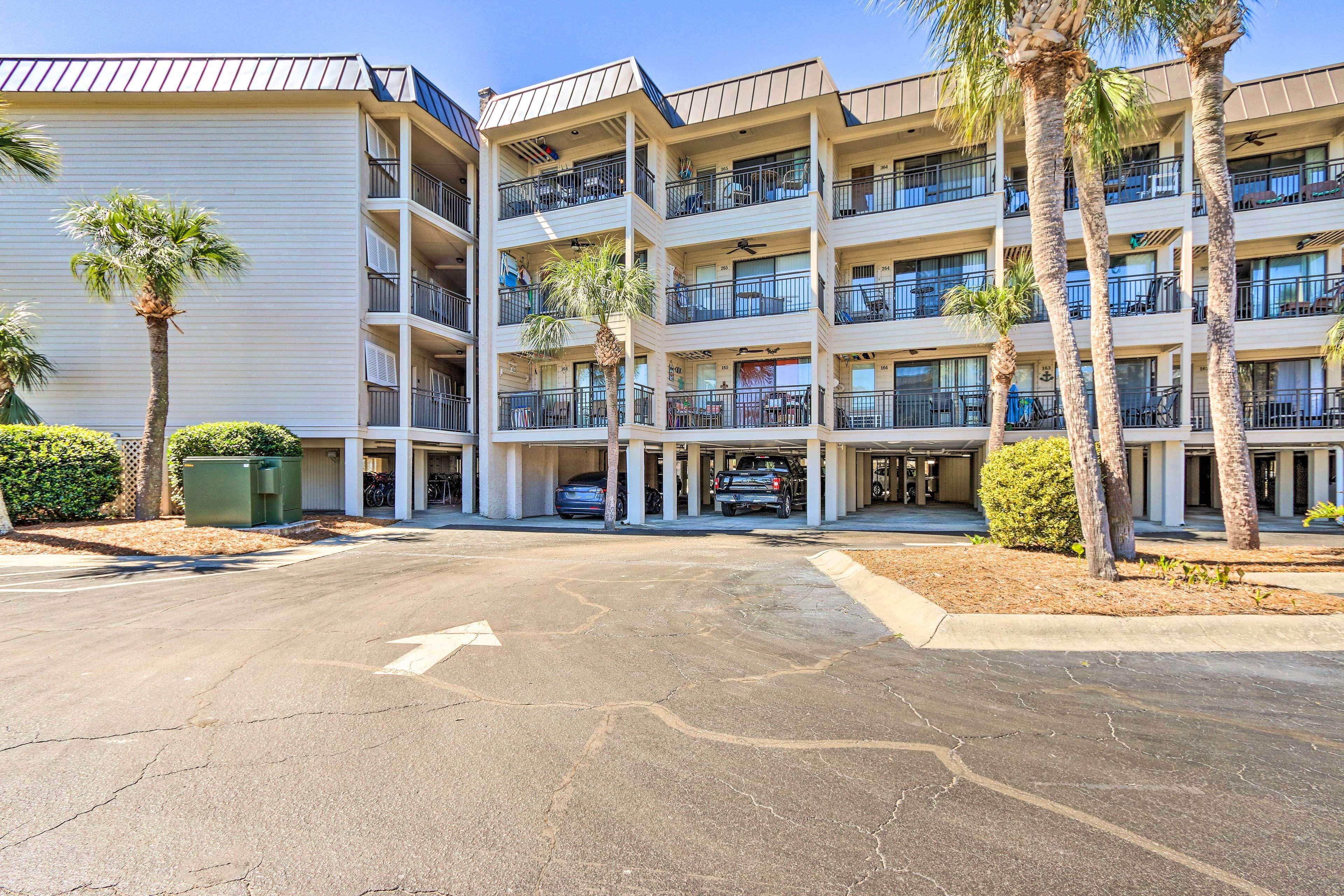 A multi-story hotel with balconies, palm trees, and a parking area.