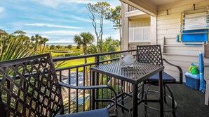 Un balcon avec une table et des chaises, donnant sur un jardin aménagé et sur des collines lointaines.