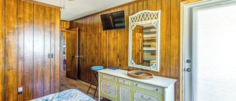 A bedroom with wooden paneling, a bed, a dresser, a mirror, and a ceiling fan.