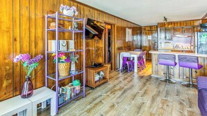 A wooden-paneled room with a white table, purple chairs, a kitchen area, and a purple shelving unit. - ~ 9 Mi to Boardwalk: Oceanfront Myrtle Beach Condo (Myrtle Beach)