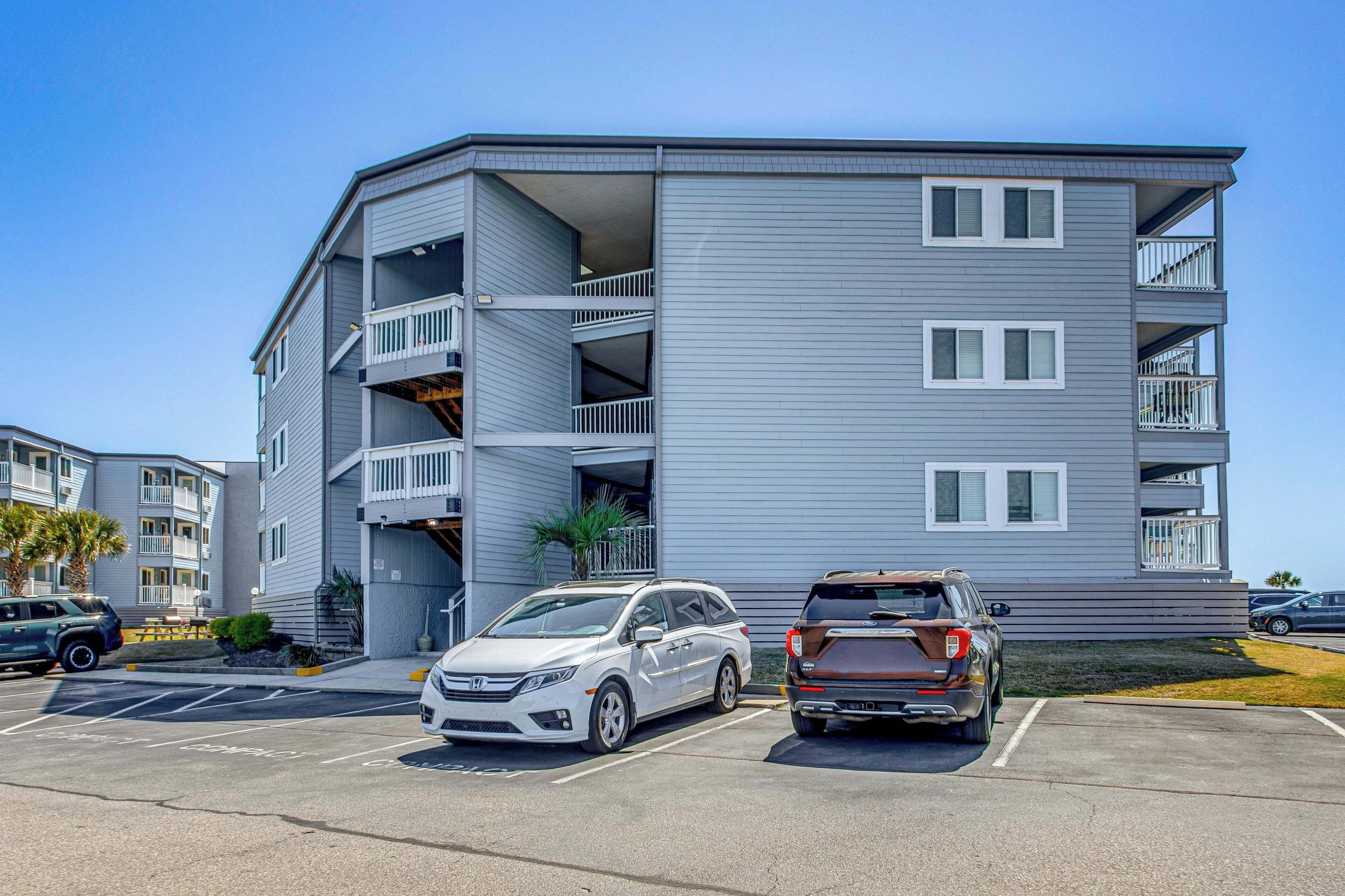 A multi-story building with balconies, parking spaces, and a clear sky.