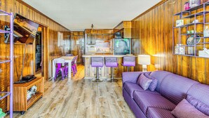 A compact kitchen with wooden cabinets, a refrigerator, and a bar area with purple stools. - ~ 9 Mi to Boardwalk: Oceanfront Myrtle Beach Condo (Myrtle Beach)