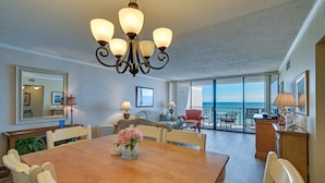 A spacious living room with a large dining table, comfortable seating, a chandelier, and a balcony with a view of the ocean. - Oceanfront Myrtle Beach Condo w/ Outdoor Pool (Myrtle Beach)