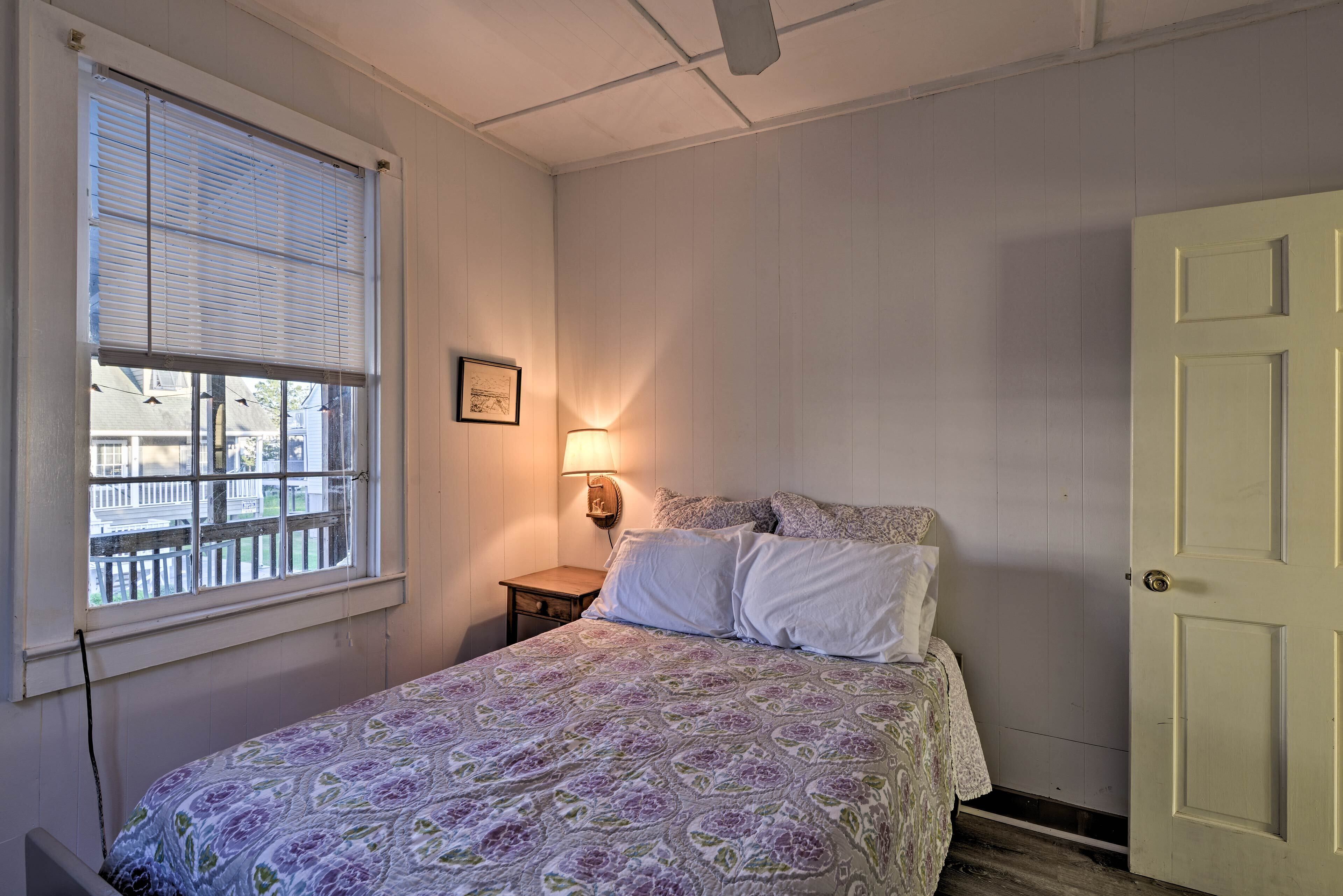 A bedroom with a bed, a window with blinds, a bedside lamp, and a door.