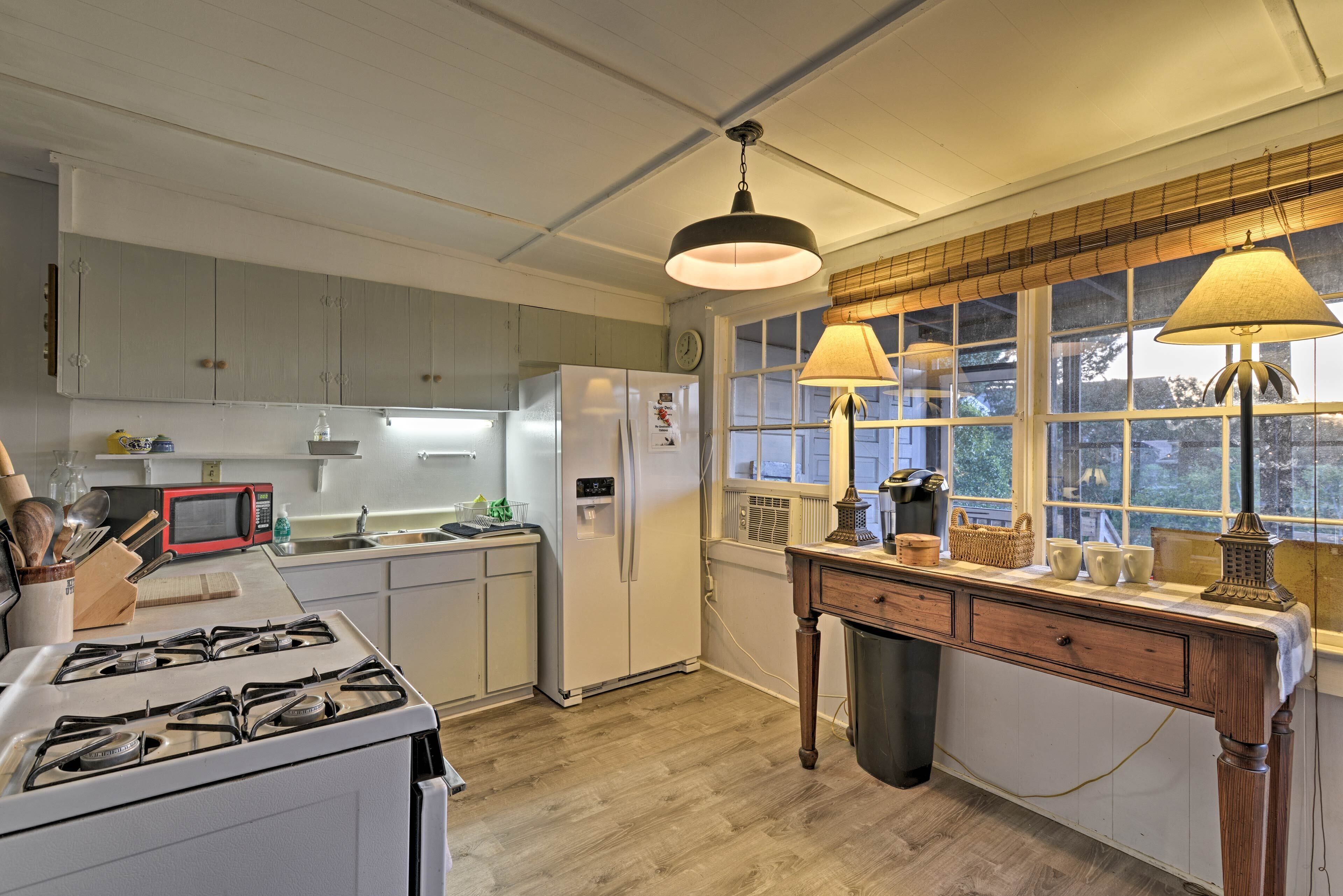 A kitchen with a gas stove, refrigerator, and wooden dining table with lamps.