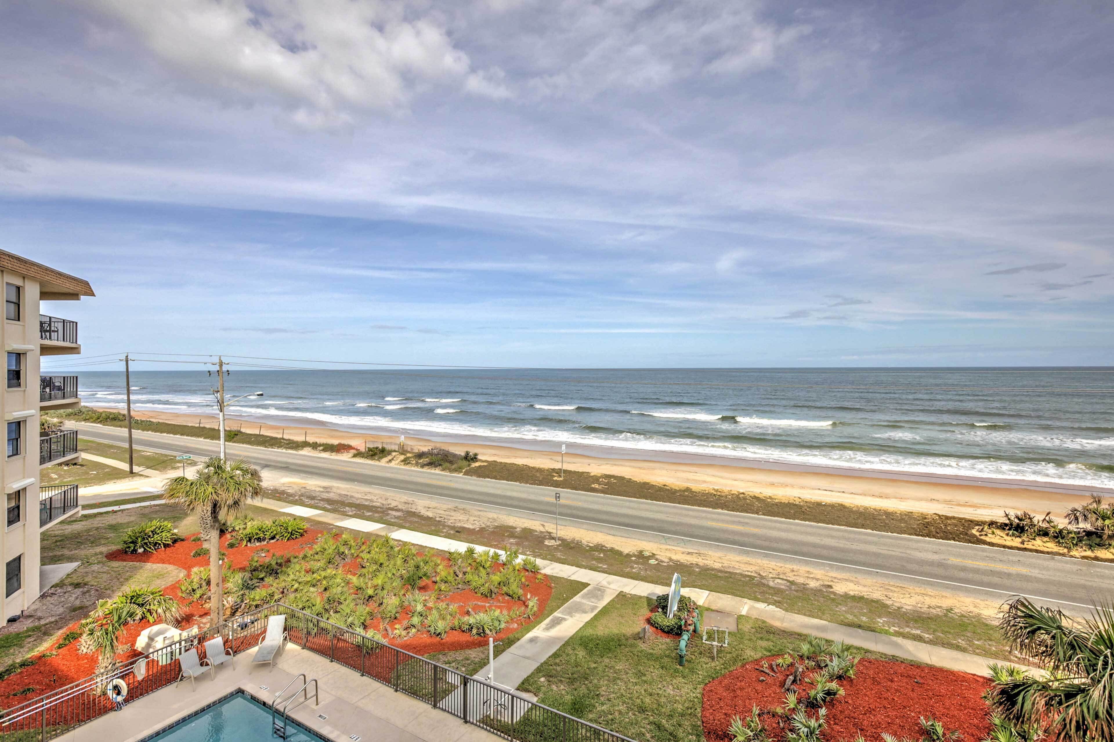 A beachfront hotel with a pool, a road leading to the beach, and a view of the ocean.