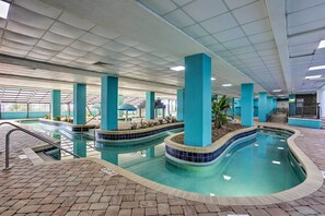 Ein Hallenbad mit Kachelwänden und einem Ziegelboden, umgeben von blauen Säulen und einer gefliesten Liegefläche.
