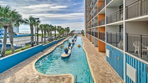Una piscina con indicador de profundidad de 0.9 metros, rodeada por un patio de ladrillo y palmeras, con un edificio con balcones al fondo.