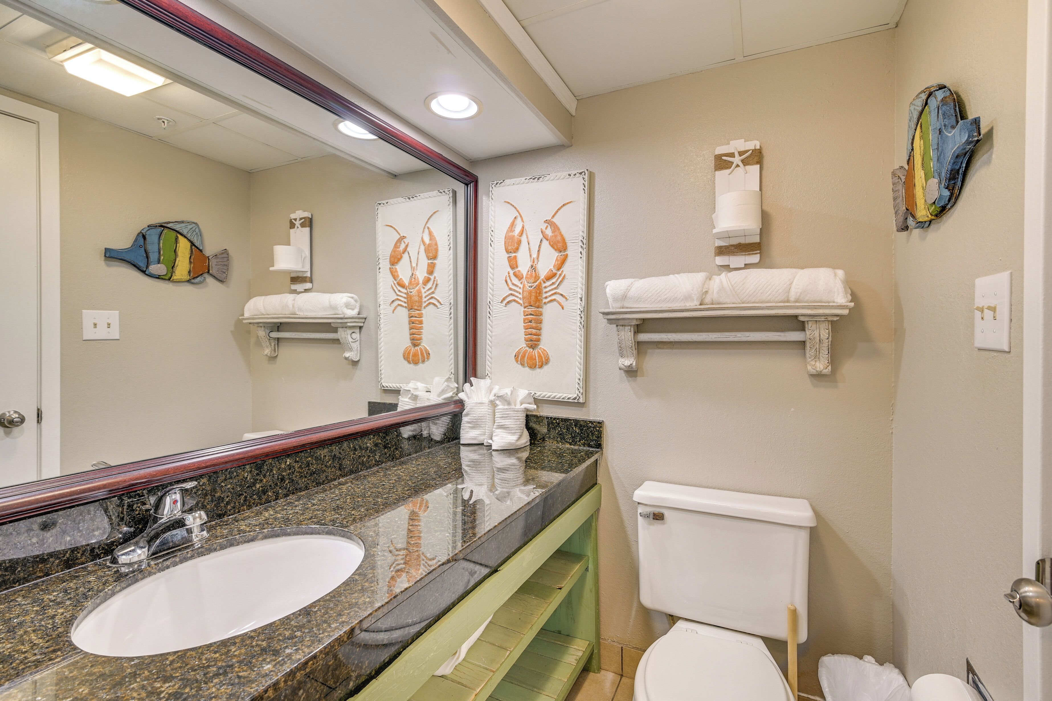A bathroom with a granite sink, white toilet, and decorative wall art.