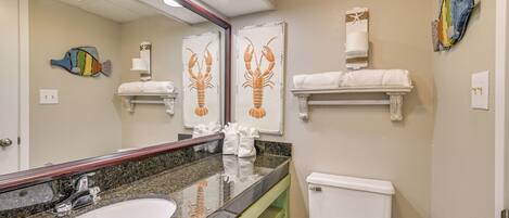 A bathroom with a granite sink, white toilet, and decorative wall art.