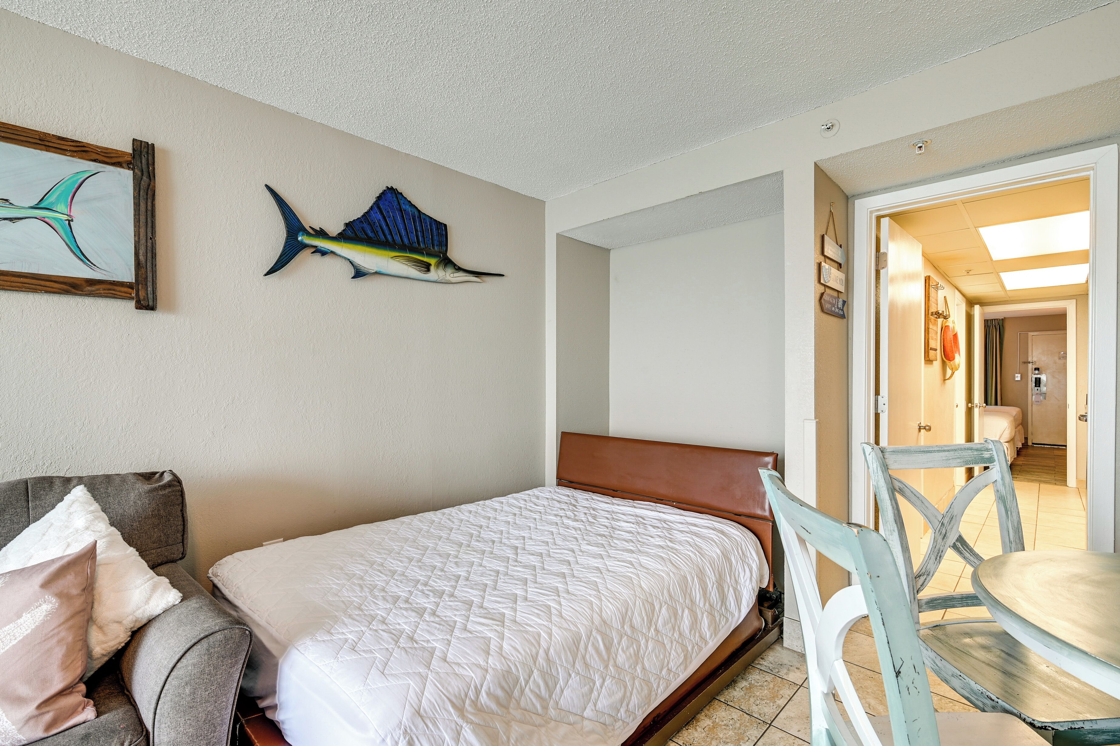 A bedroom with a bed, a gray couch, a wooden headboard, a chair, and a wall-mounted fish decoration.