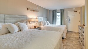 A hotel room with two beds, a nightstand with a lamp, a dresser, and a door with a lock. - Oceanfront Balcony: Resort Condo in Myrtle Beach (Myrtle Beach)
