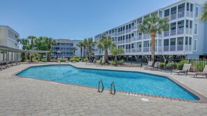 Une piscine entourée de chaises longues et de palmiers, le tout bordé d’un immeuble à plusieurs étages doté de balcons.