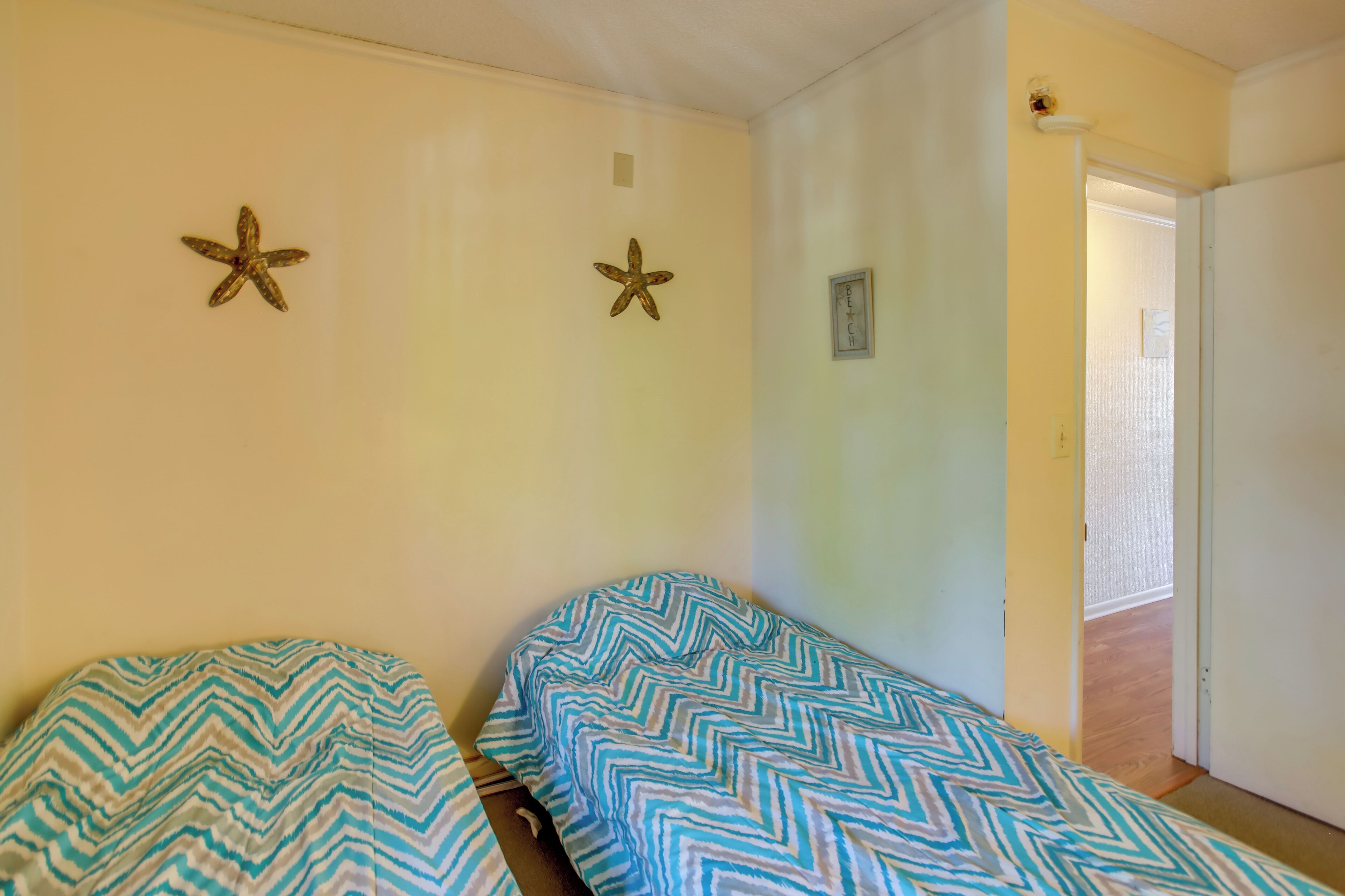 A room with two beds, each with a zigzag patterned bedspread. There are starfish decorations on the wall and a small framed picture.