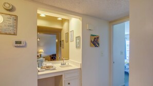 Une salle de bain avec un lavabo blanc, un miroir et un thermostat fixé au mur.
