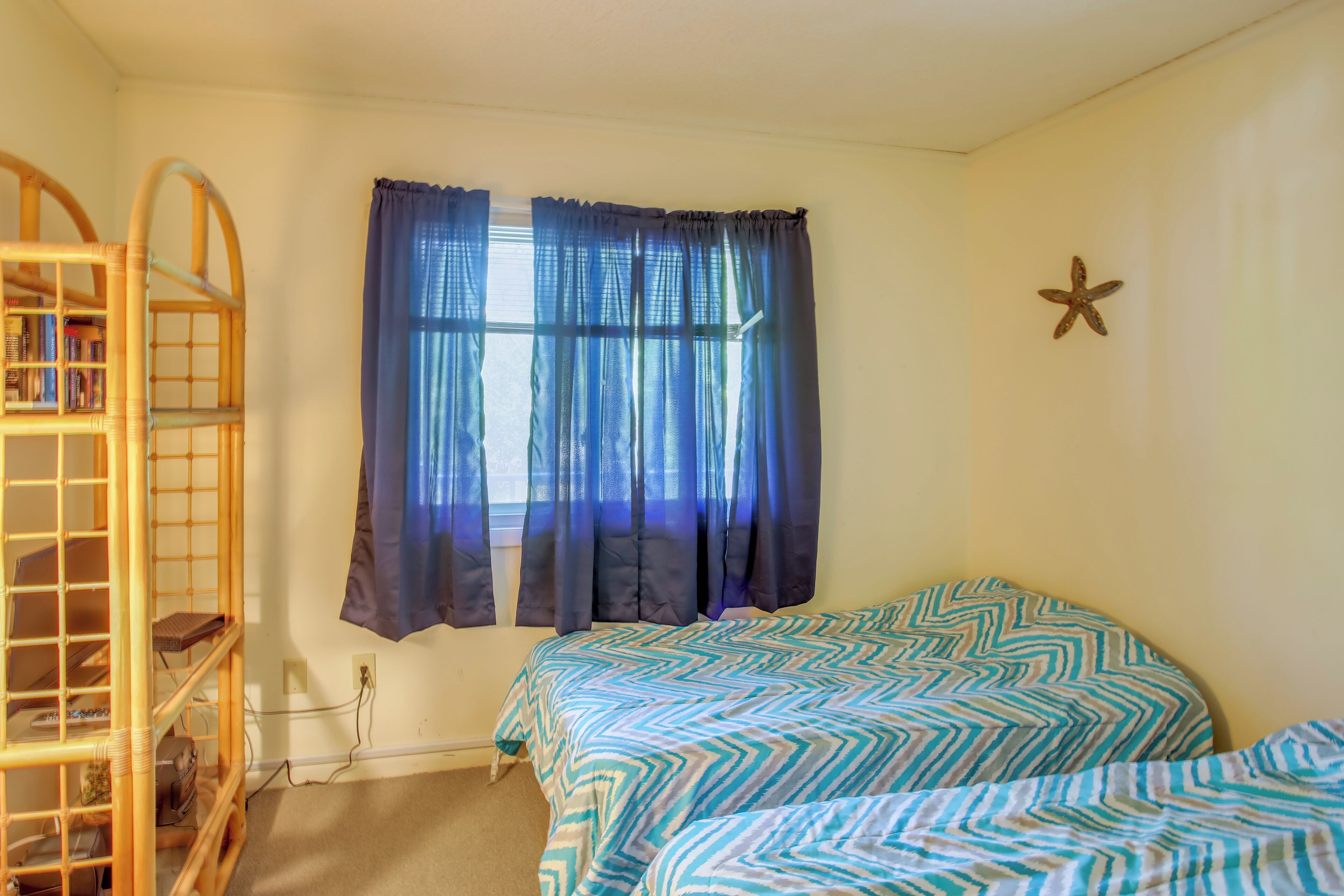 Une chambre avec un lit superposé, une fenêtre avec des rideaux bleus et une décoration en forme d’étoile de mer sur le mur.