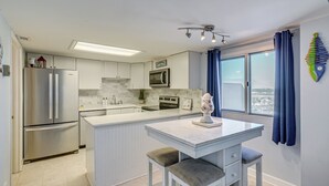 A modern kitchen with white cabinetry, a stainless steel refrigerator, a microwave, and a large island with bar stools.