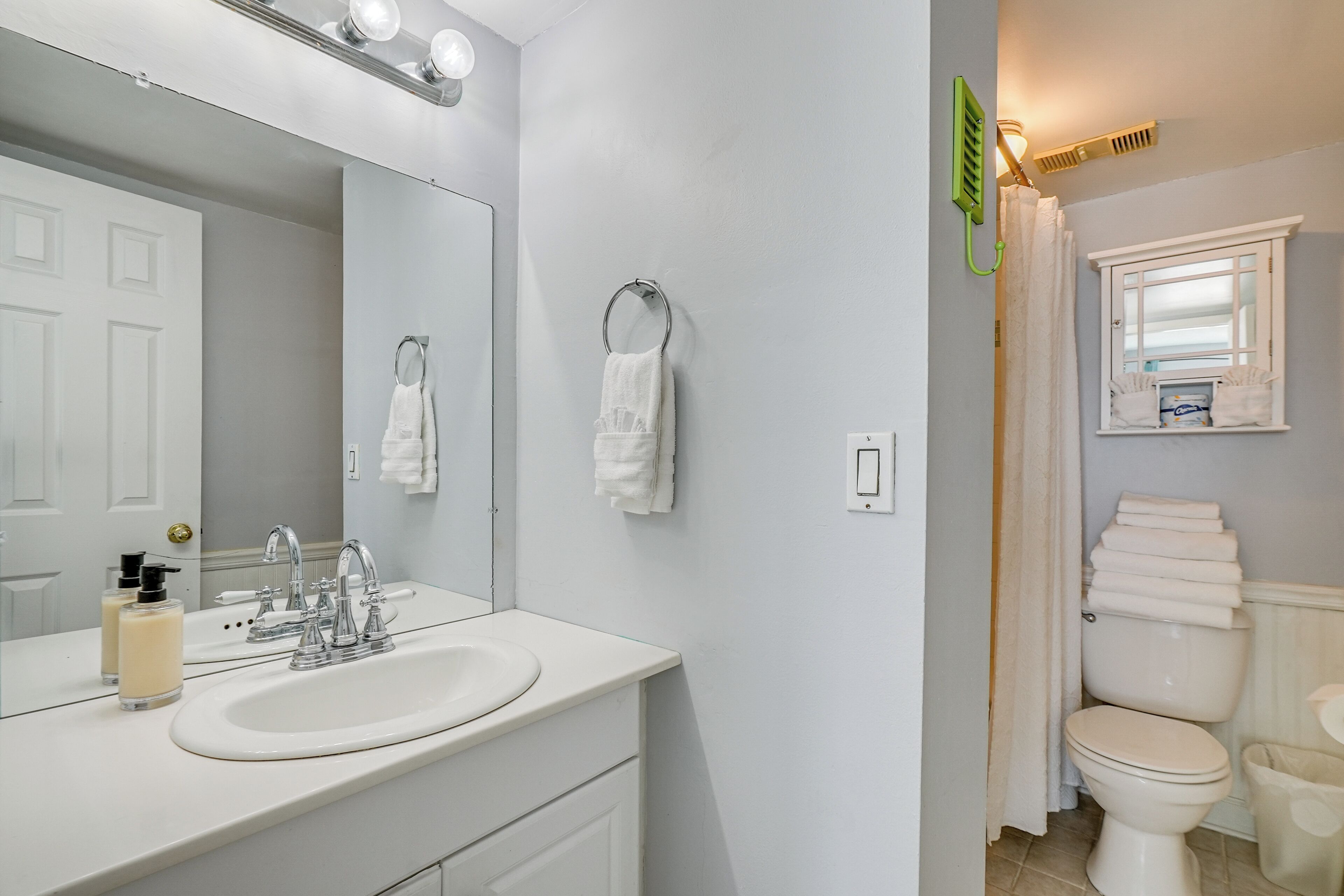 A bathroom with a white sink, mirror, and toilet. There are two towels hanging on the wall.